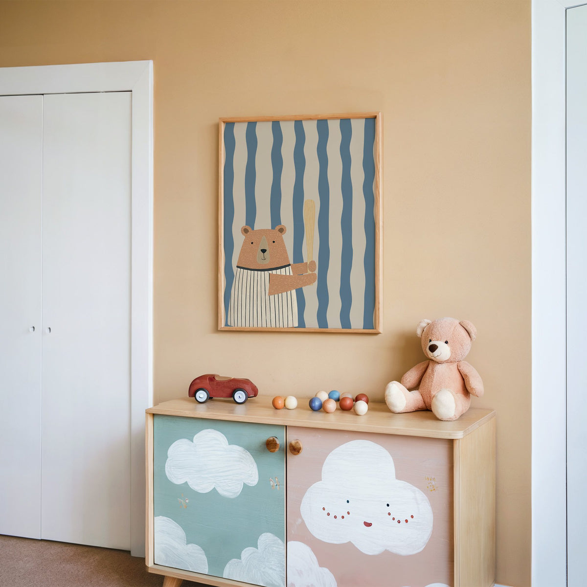 Baseball bear blue stripe nursery print in an oak frame on a peach wall above a cloud-painted cabinet