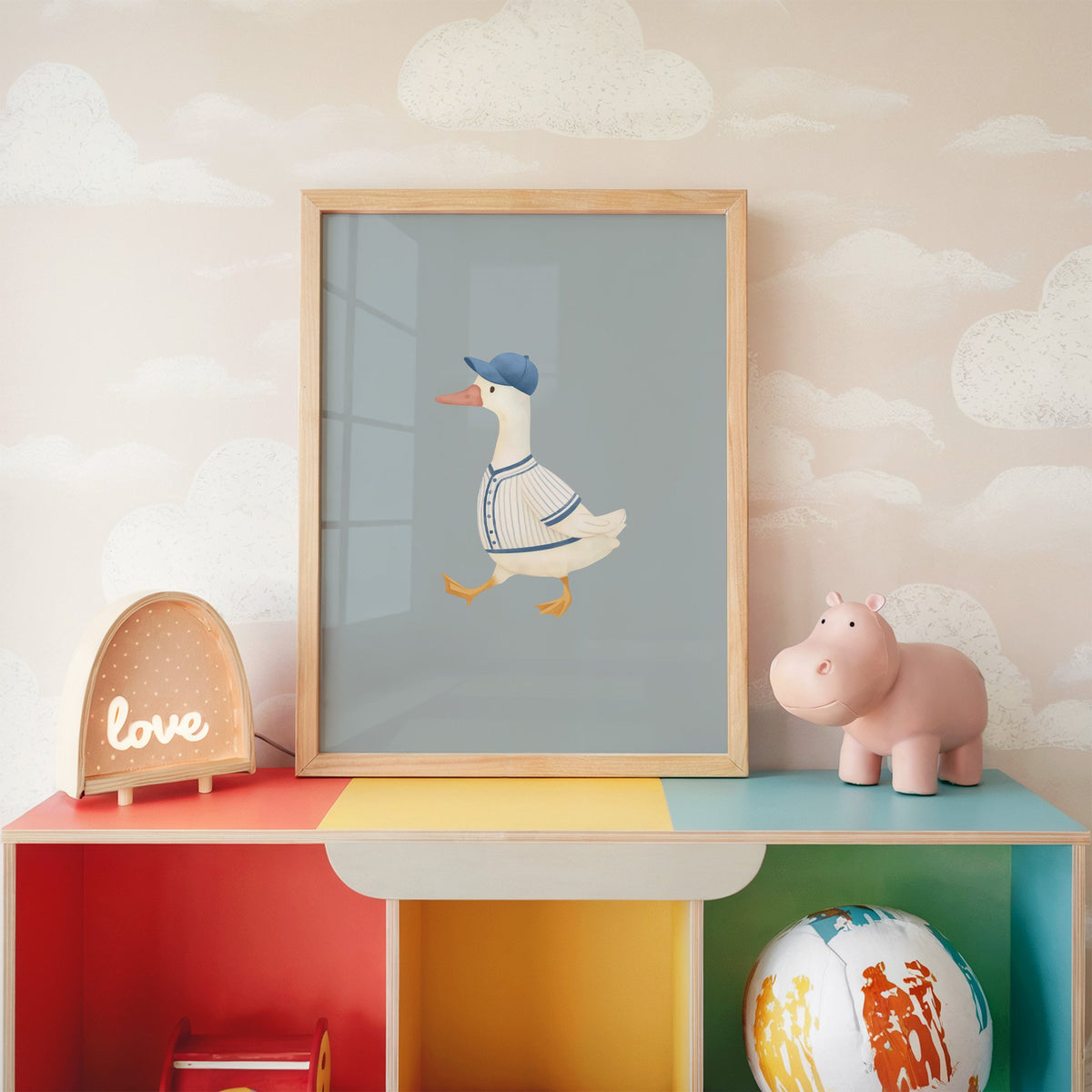 Baseball bird blue cap nursery print in an oak frame on a rainbow toy shelf against cloud wallpaper