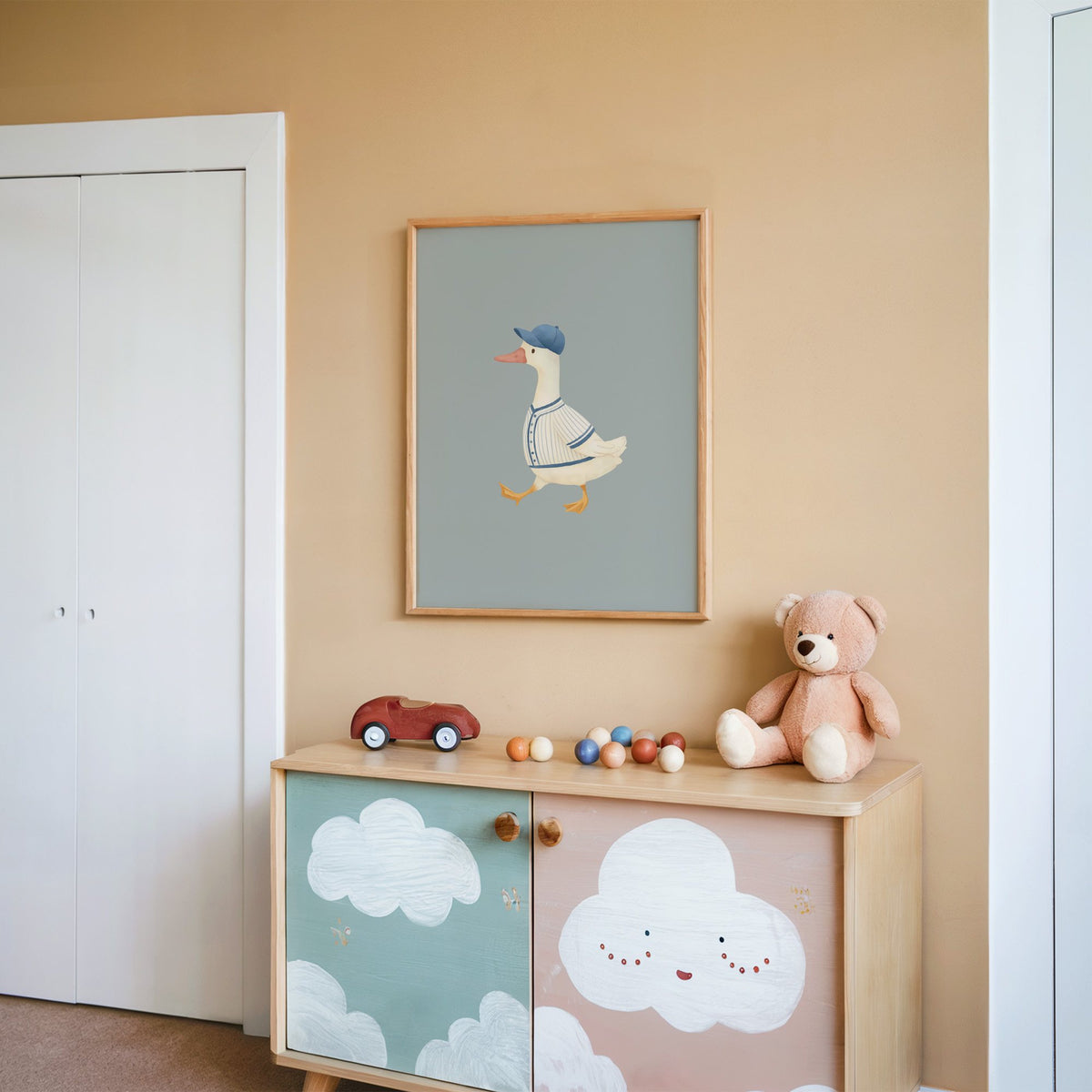 Baseball bird blue cap nursery print in an oak frame on a peach wall above a cloud-painted cabinet