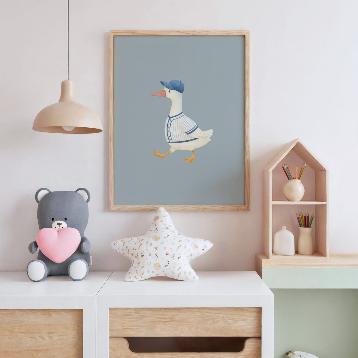 Baseball bird blue cap nursery print in an oak frame above a white dresser with a star pillow and house shelf