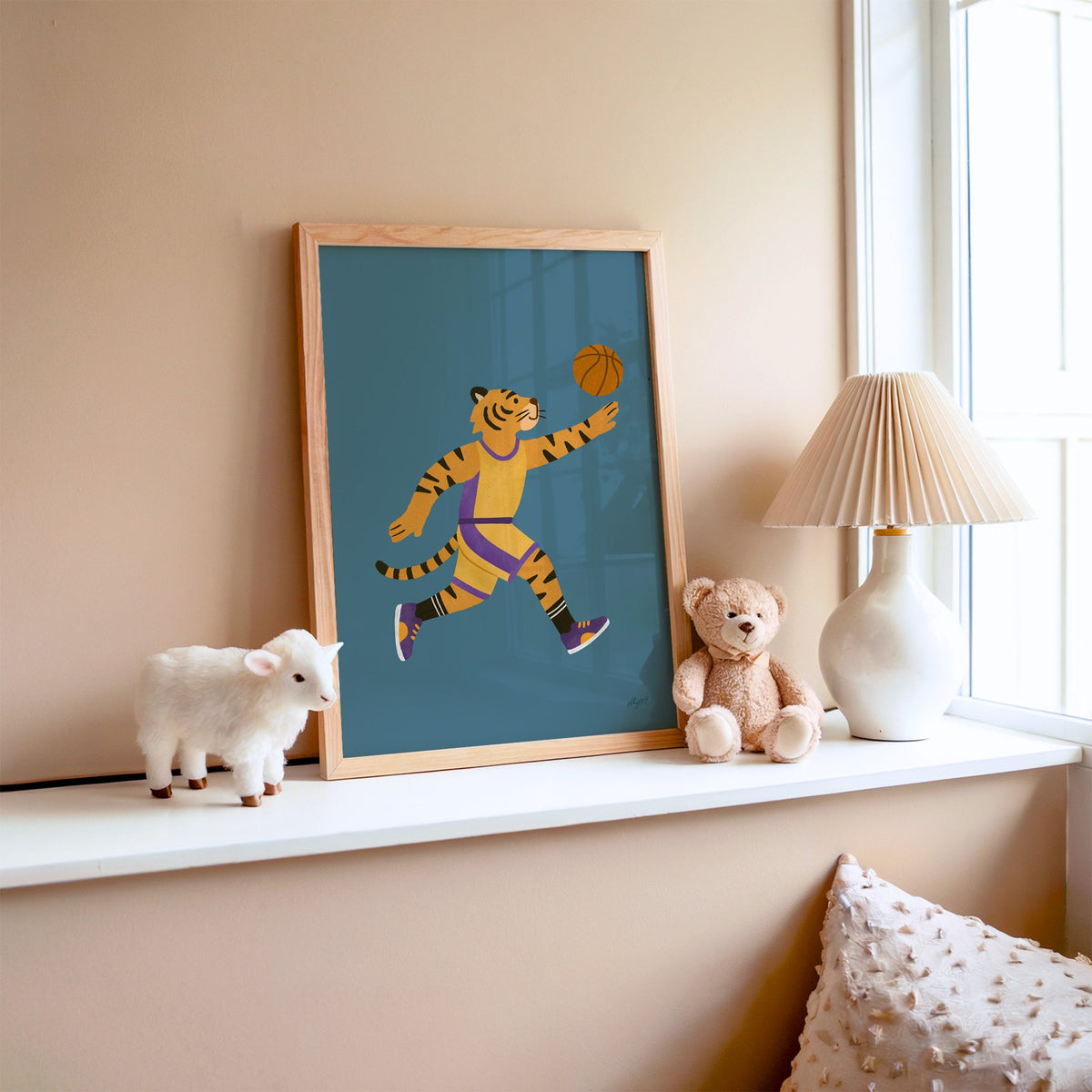 Tiger playing basketball nursery print in an oak frame on a window ledge with a toy lamb and teddy