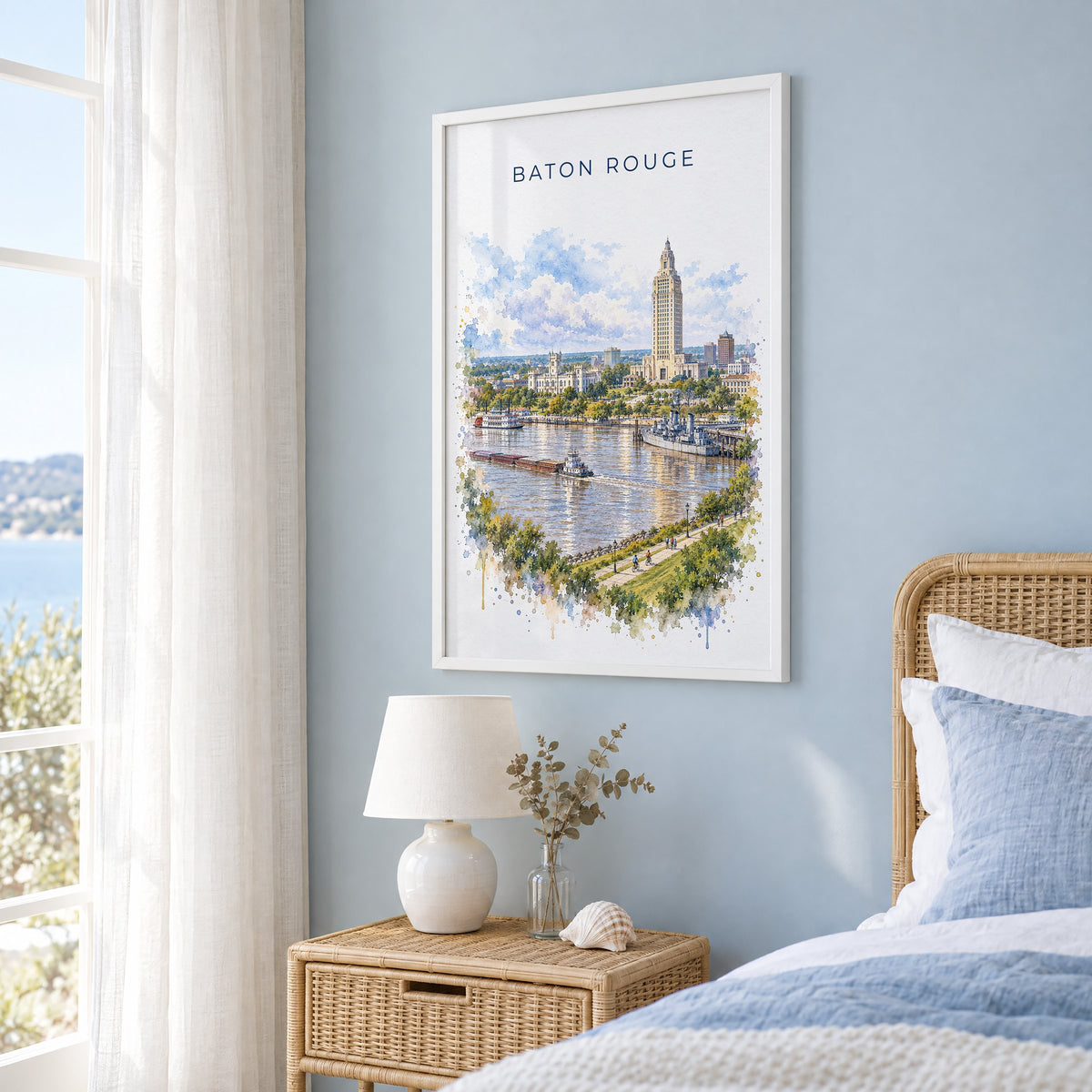 Baton Rouge watercolor print in a white frame on a pale blue wall beside a rattan bed in a coastal bedroom