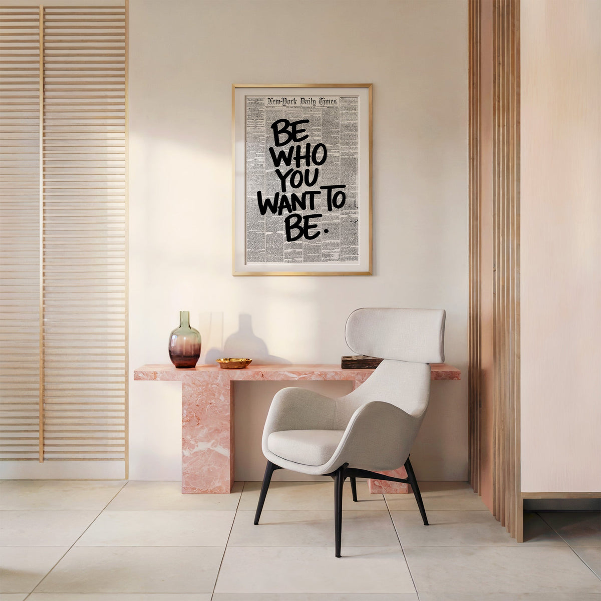 Brush lettering over vintage newspaper page print shown in a gold frame above a pink marble console and armchair