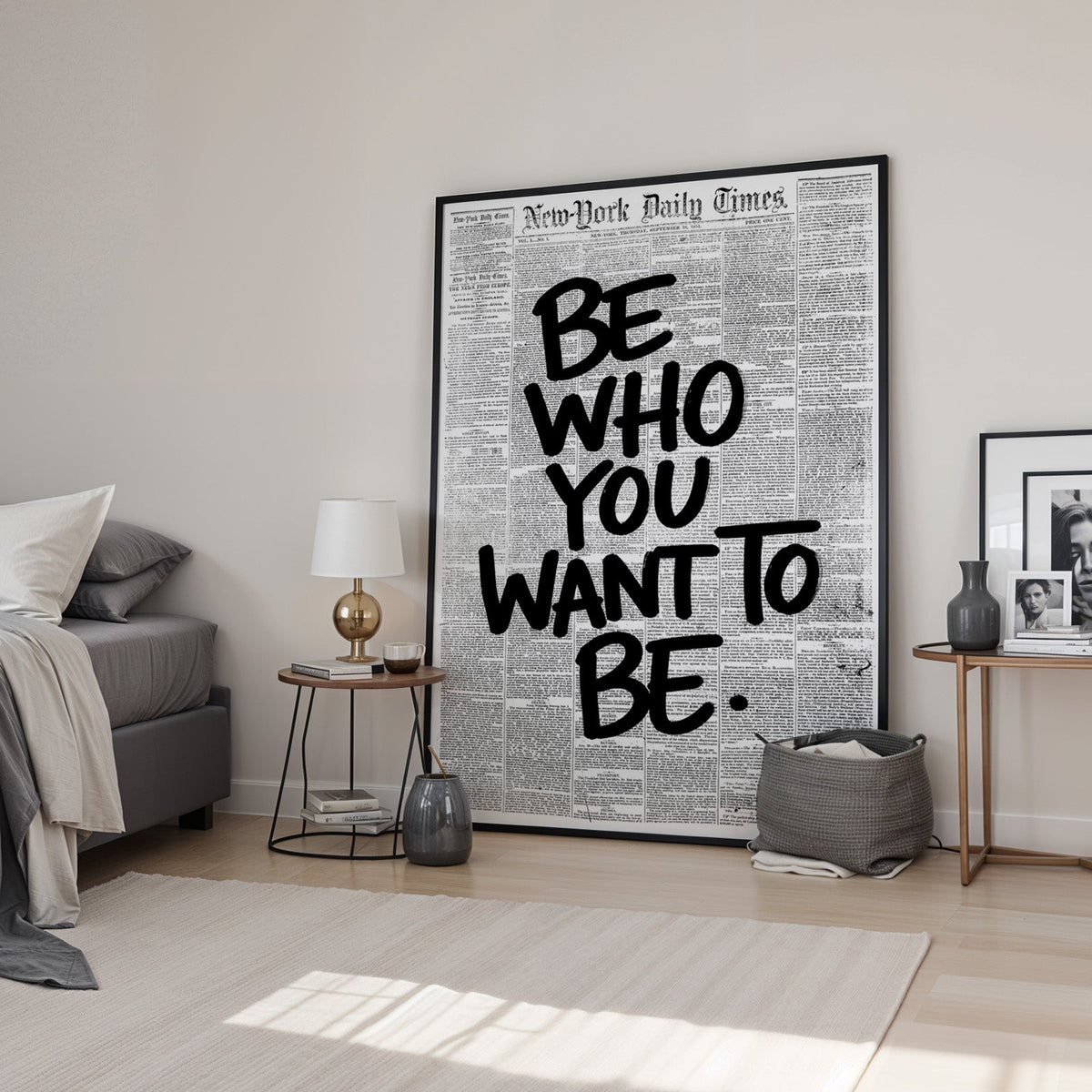 Brush lettering over vintage newspaper page print in a black frame leaning in a bedroom beside a gold lamp