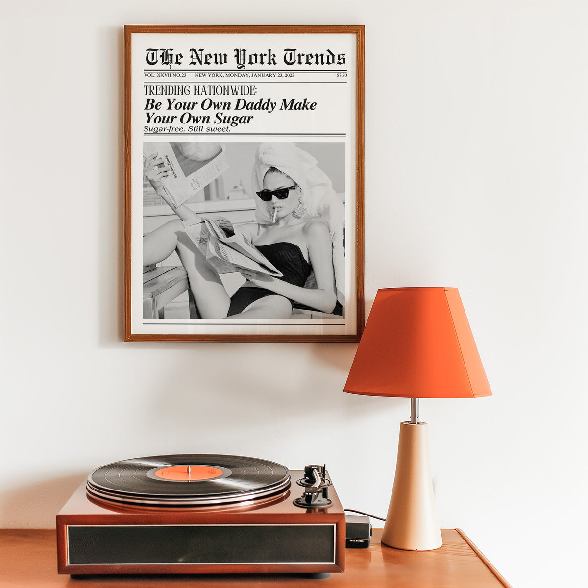 Woman reading newspapers on rooftop mock front page print in a walnut frame above a record player and orange lamp