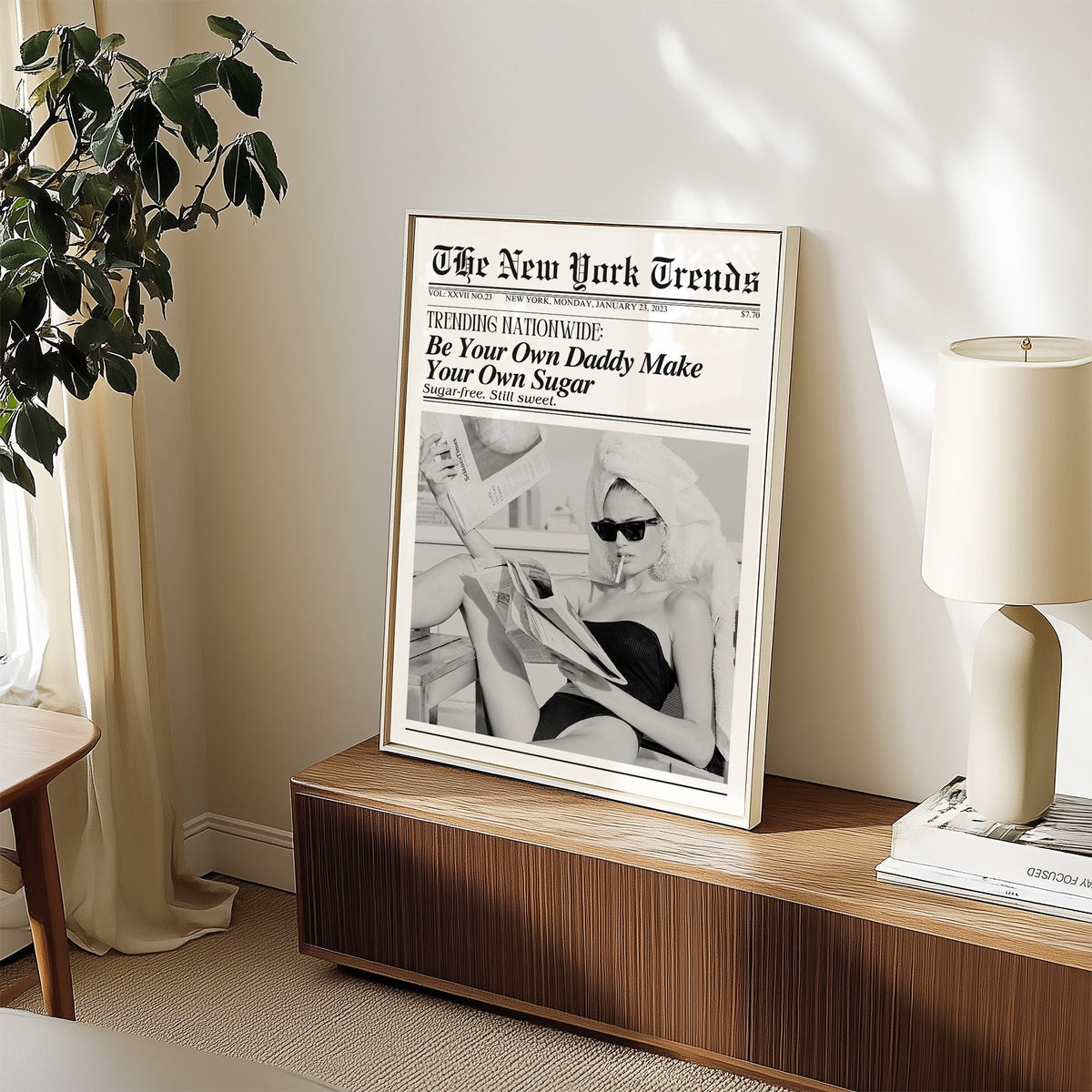 Woman reading newspapers on rooftop mock front page print in a white frame on a walnut sideboard beside a ceramic lamp