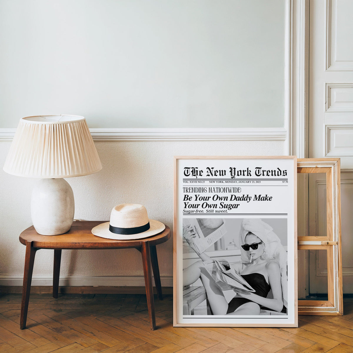 Woman reading newspapers on rooftop mock front page print in a pine frame on a wood floor beside a lamp and straw hat