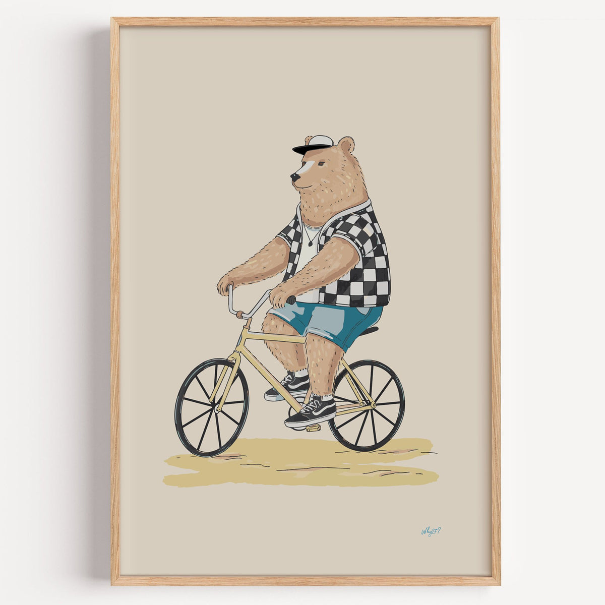 Brown bear riding yellow bicycle nursery print in a light oak frame on a plain white wall