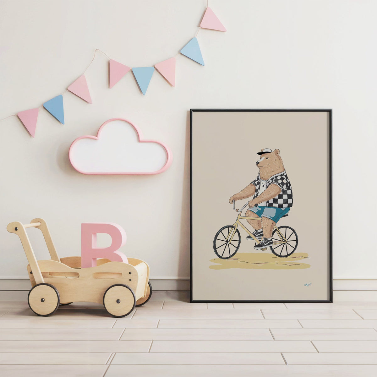 Brown bear riding yellow bicycle nursery print in a black frame under pastel bunting by a wooden baby walker
