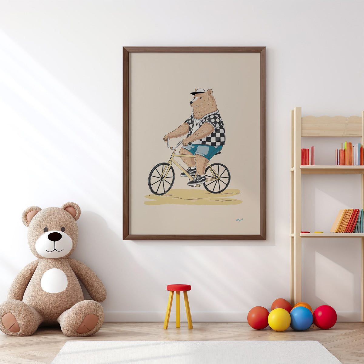 Brown bear riding yellow bicycle nursery print in a walnut frame above a big teddy bear by a bookshelf
