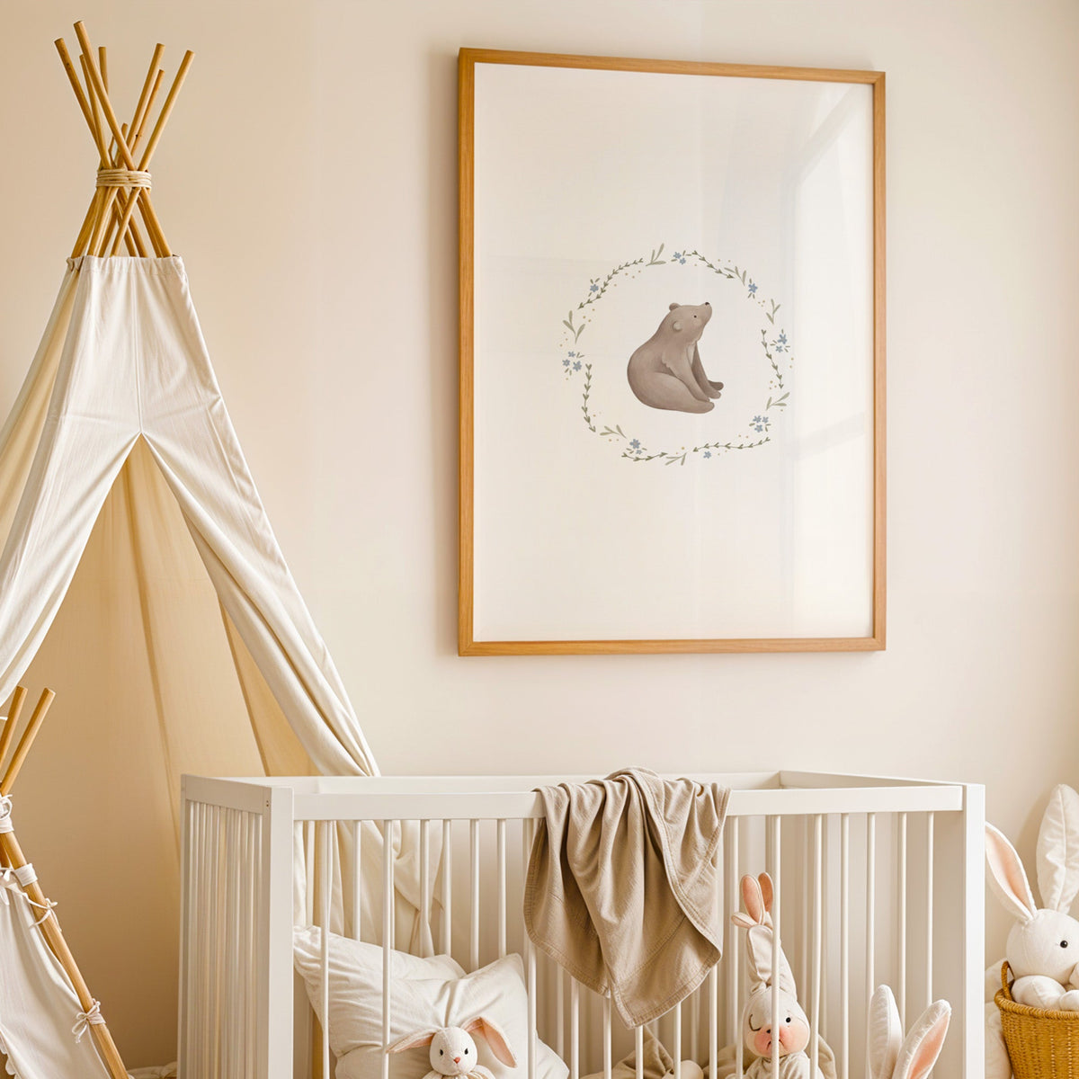 Bear cub in a blue flower wreath nursery print in an oak frame above a white crib beside a canvas teepee