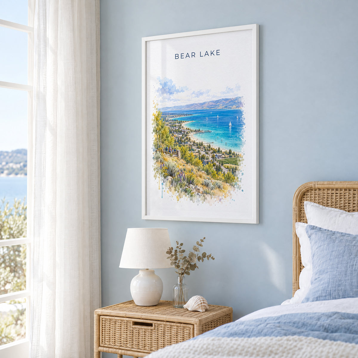 Bear Lake watercolor print in a white frame on a pale blue wall beside a rattan bed in a coastal bedroom