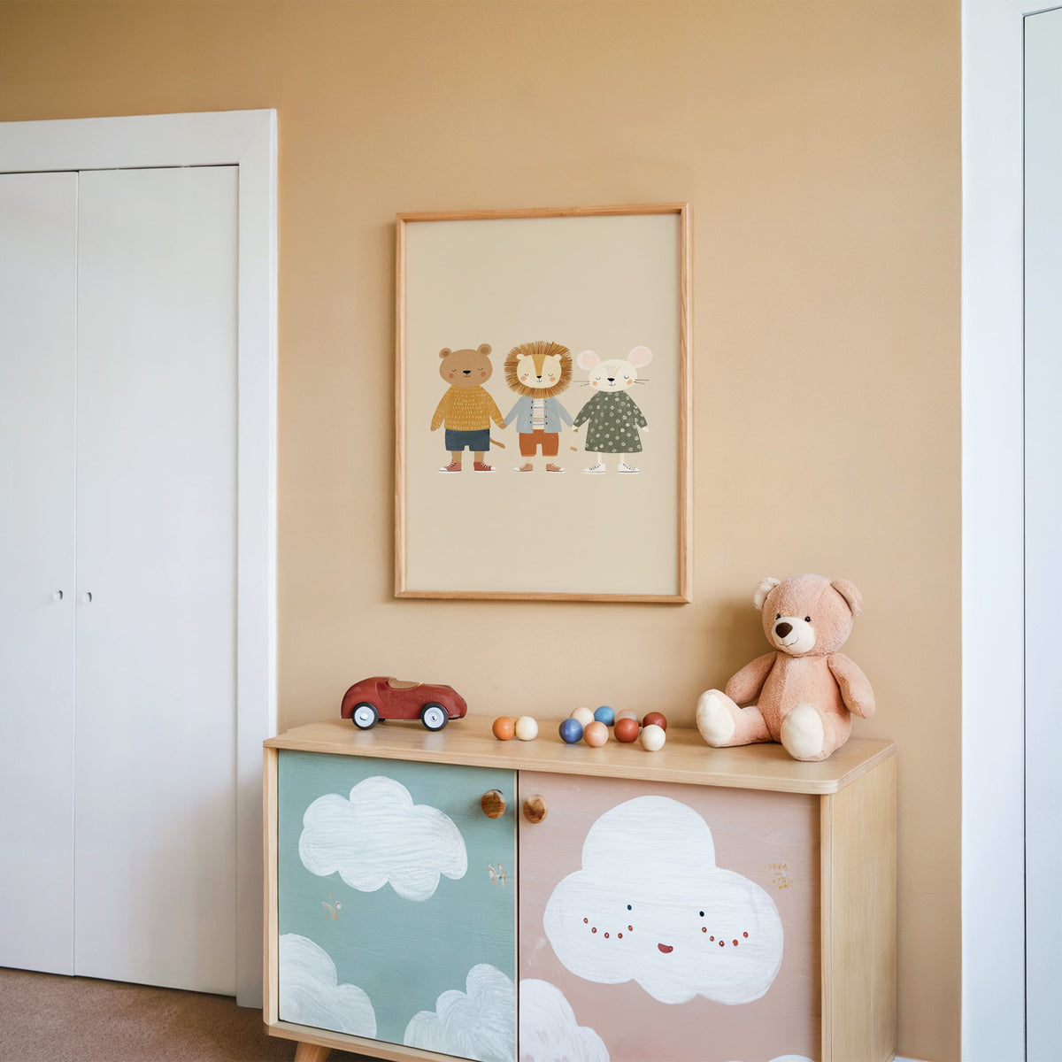 Three friends holding hands nursery print in an oak frame on a peach wall above a cloud-painted cabinet