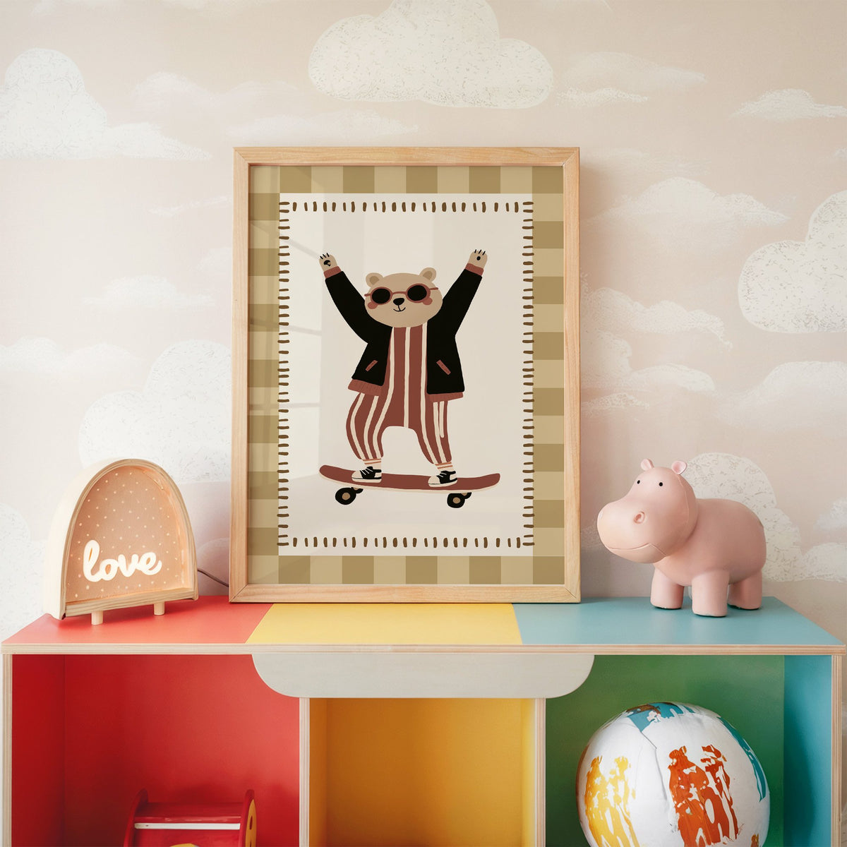 Skateboard bear checker border nursery print in an oak frame on a rainbow toy shelf against cloud wallpaper