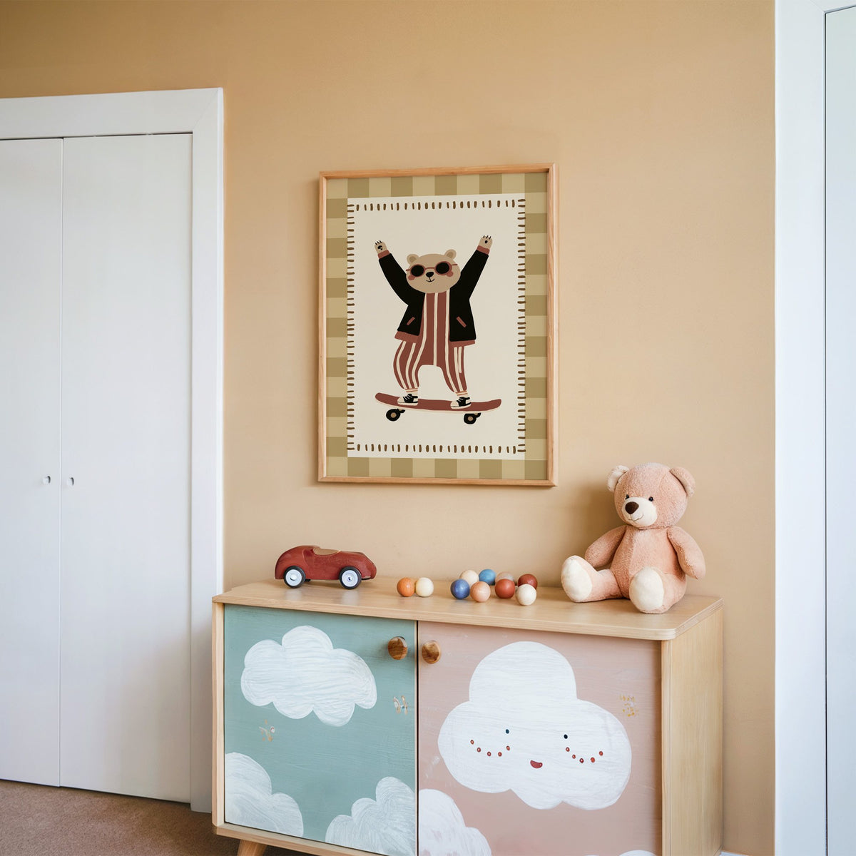 Skateboard bear checker border nursery print in an oak frame on a peach wall above a cloud-painted cabinet