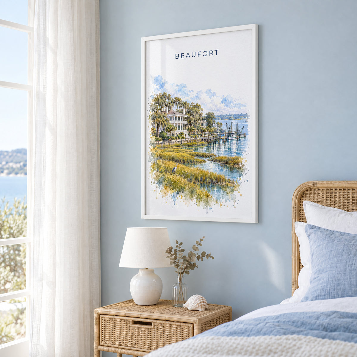 Beaufort, South Carolina watercolor print in a white frame on a pale blue wall beside a rattan bed in a coastal bedroom
