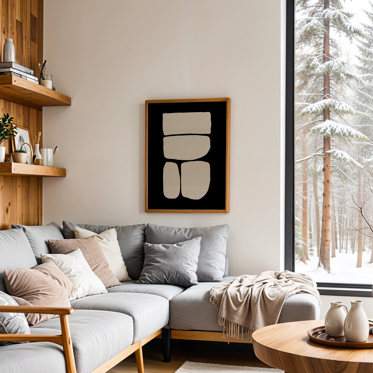 Beige four stacked stones on black minimalist print in an oak frame above a grey sectional sofa by a snowy forest window