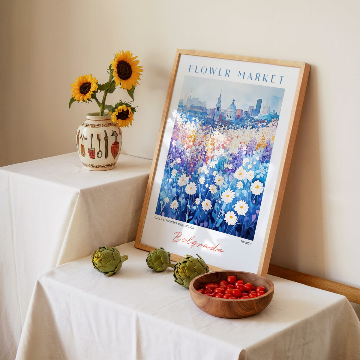 Belgrade flower market print in an oak frame leaning on a linen-draped table beside a vase of sunflowers