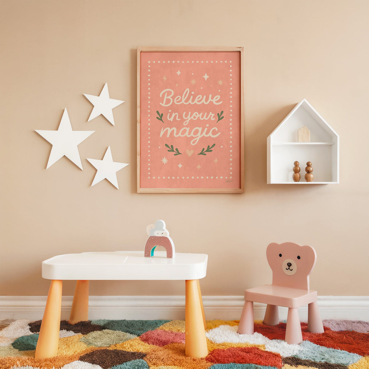 Believe in your magic coral quote nursery print in an oak frame on a peach wall above a kids table with wall stars
