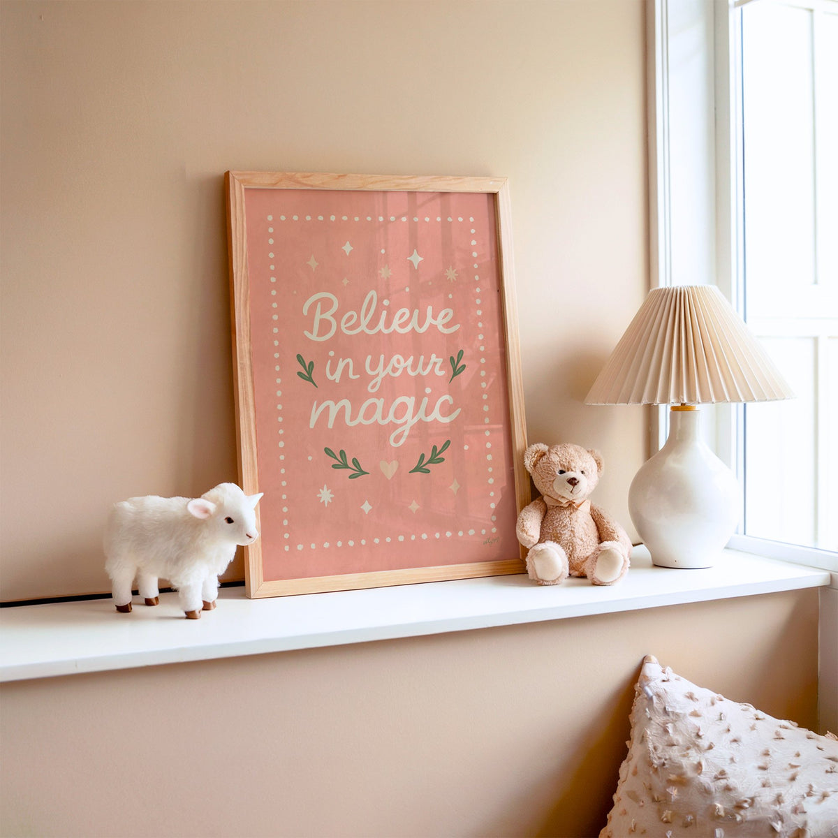 Believe in your magic coral quote nursery print in an oak frame on a window ledge with a toy lamb and teddy