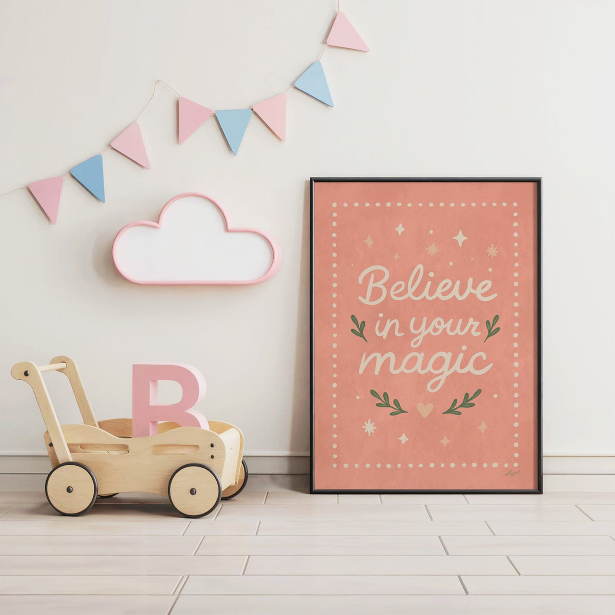 Believe in your magic coral quote nursery print in a black frame under pastel bunting by a wooden baby walker