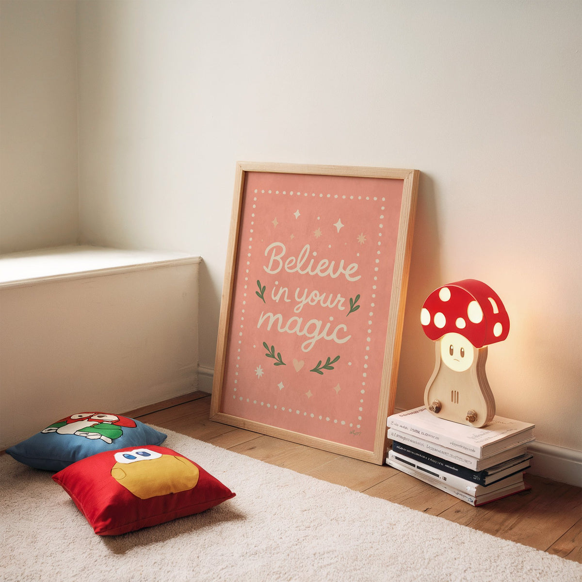 Believe in your magic coral quote nursery print in an oak frame leaning on a rug beside a mushroom lamp and floor cushions