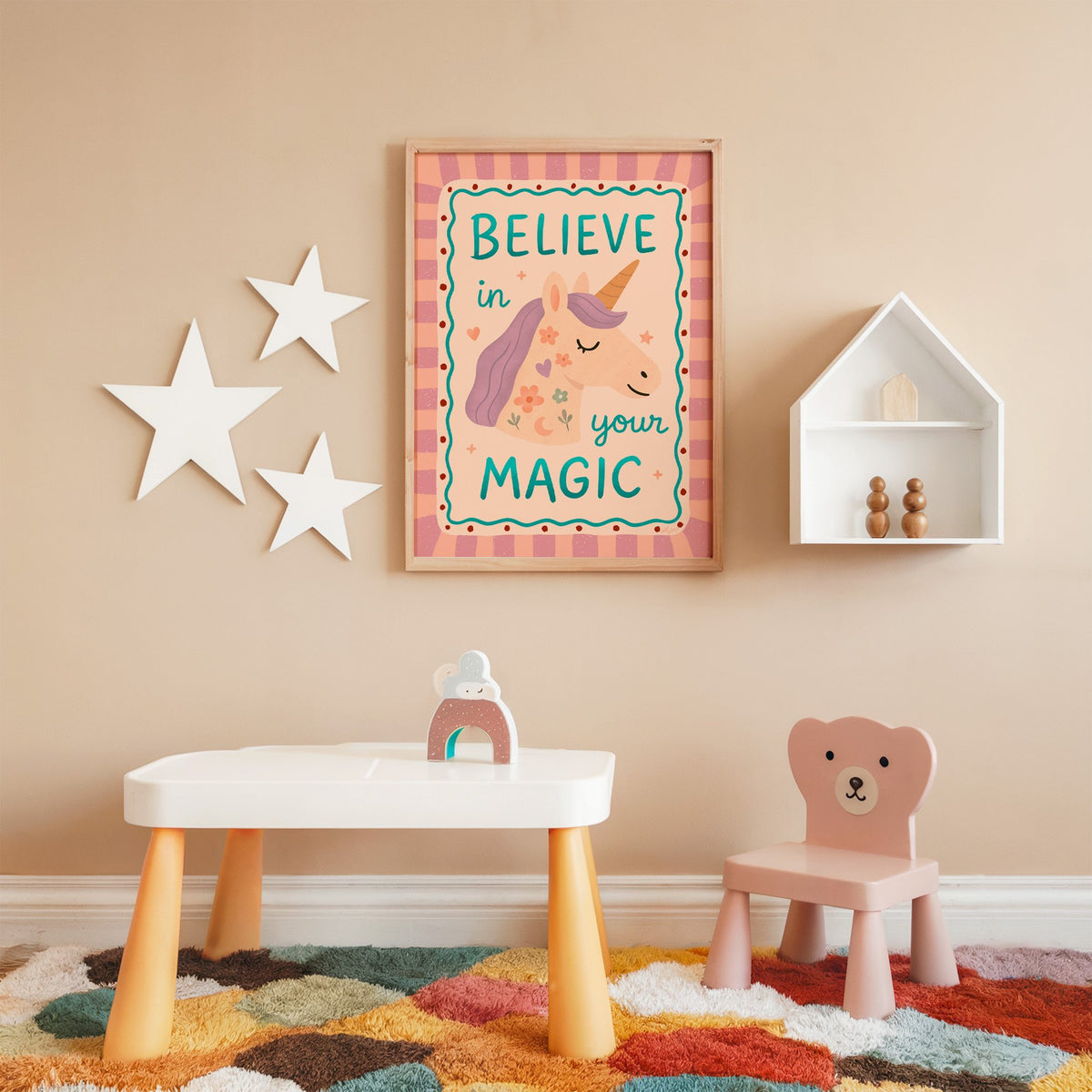 Believe in your magic unicorn nursery print in an oak frame on a peach wall above a kids table with wall stars