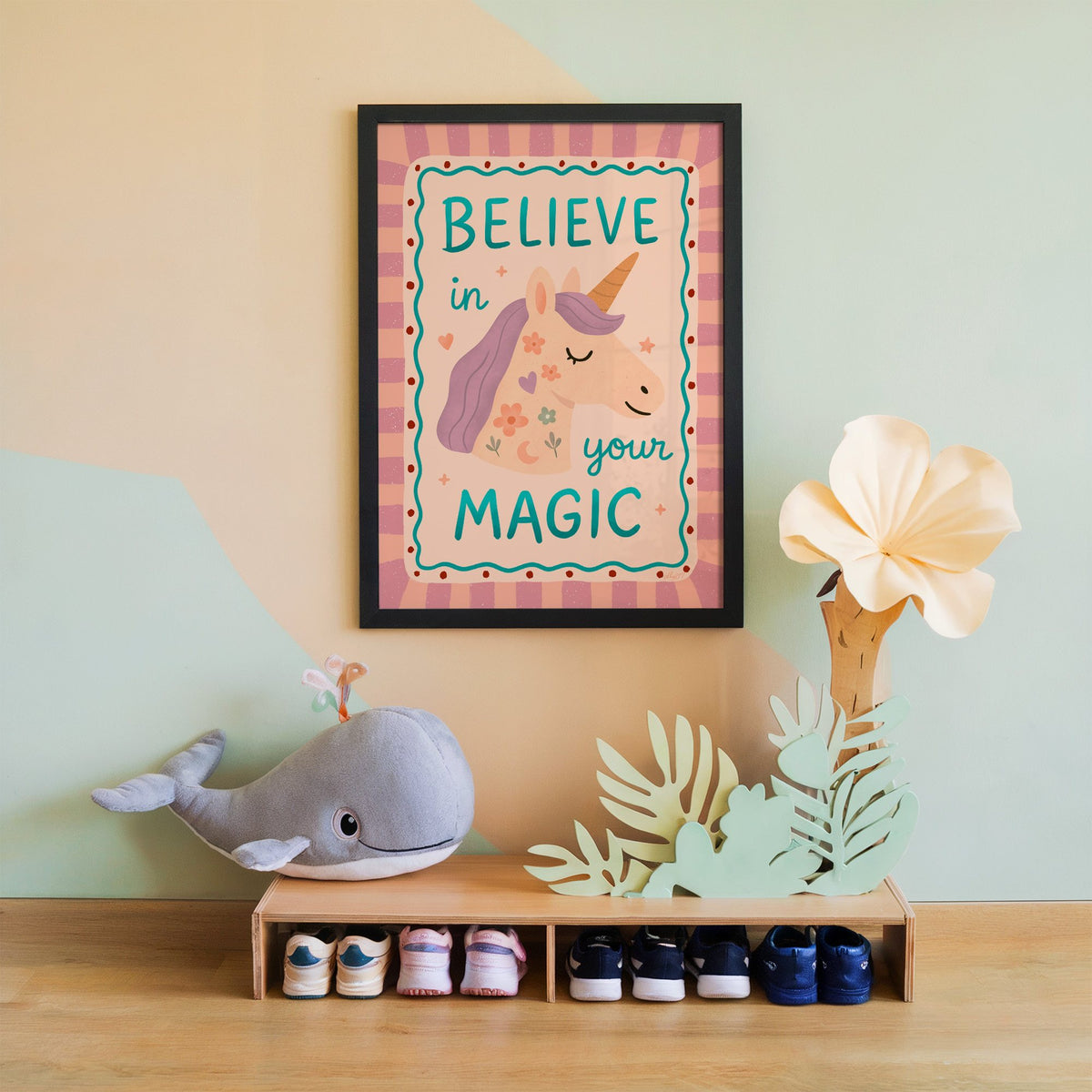 Believe in your magic unicorn nursery print in a black frame on a mint and peach wall above a whale plush