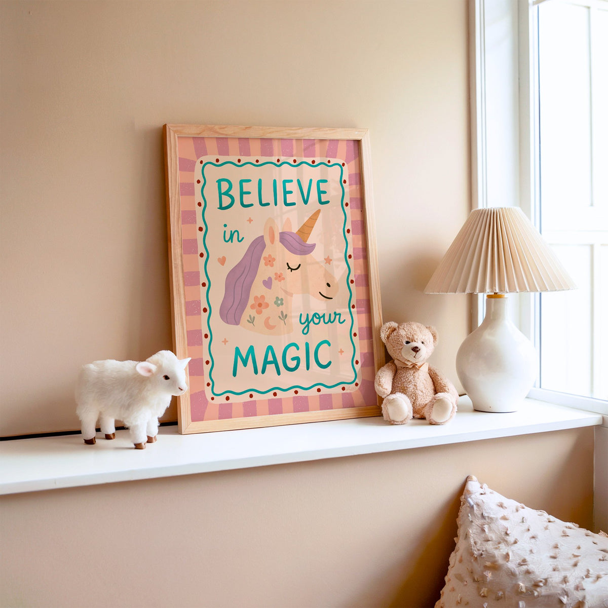 Believe in your magic unicorn nursery print in an oak frame on a window ledge with a toy lamb and teddy