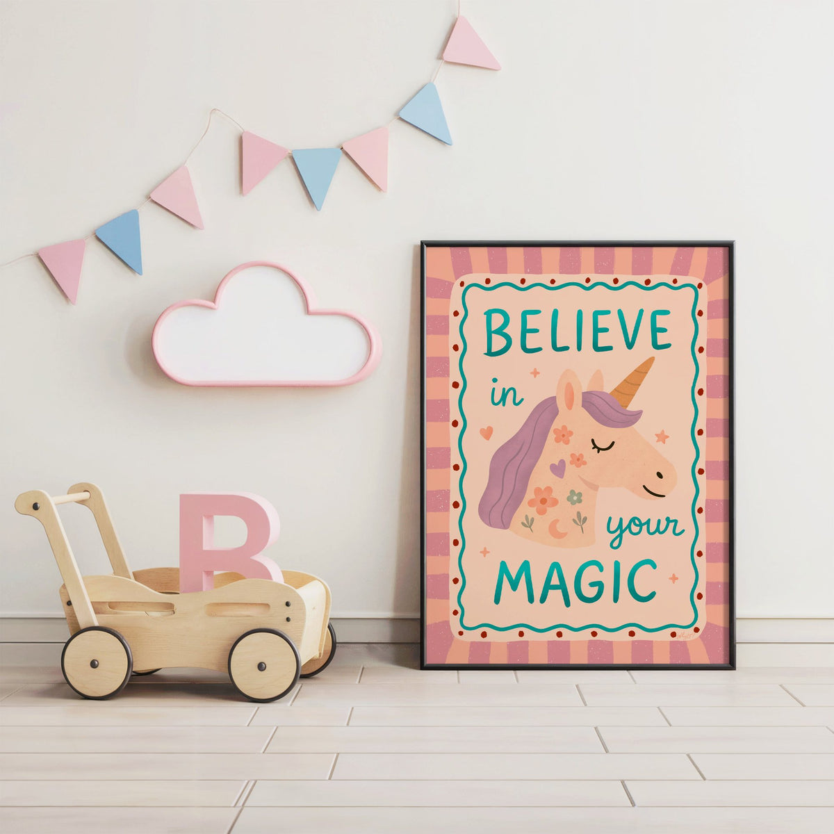 Believe in your magic unicorn nursery print in a black frame under pastel bunting by a wooden baby walker