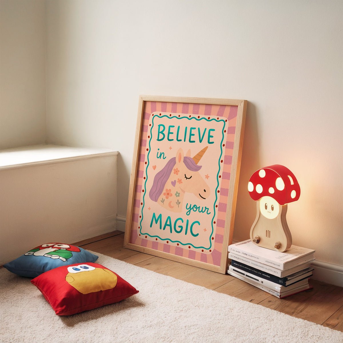 Believe in your magic unicorn nursery print in an oak frame leaning on a rug beside a mushroom lamp and floor cushions