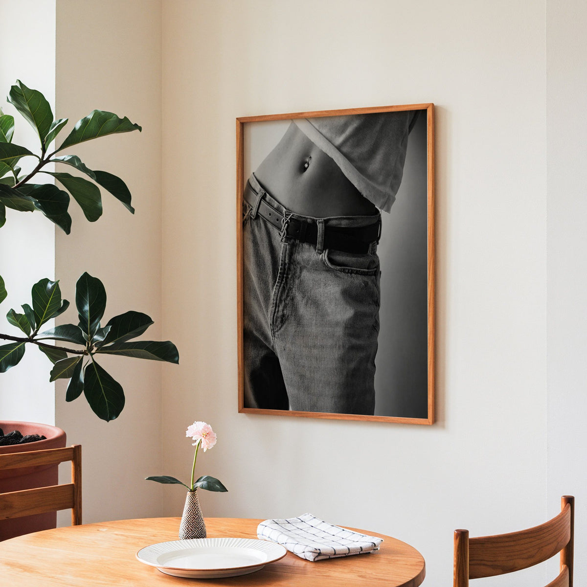 Belly piercing above faded jeans and belt buckle print in a teak frame above a round wooden dining table