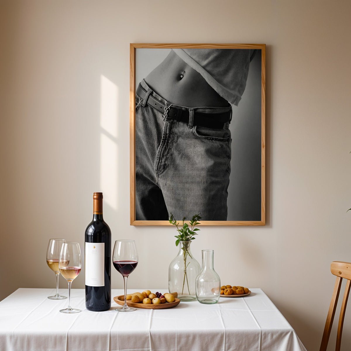Belly piercing above faded jeans and belt buckle print in an oak frame above a table set with red wine and glasses