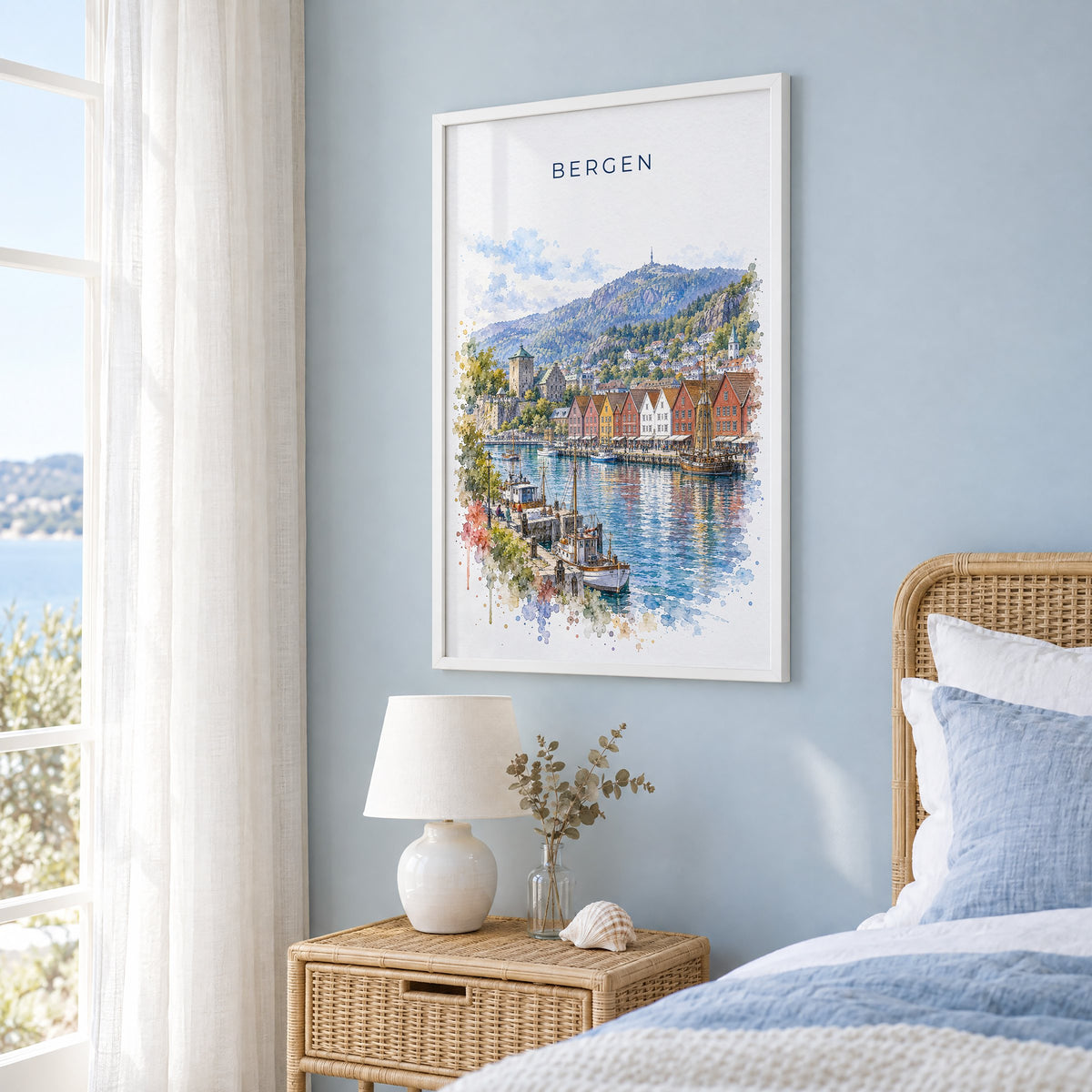 Bergen, Norway watercolor print in a white frame on a pale blue wall beside a rattan bed in a coastal bedroom