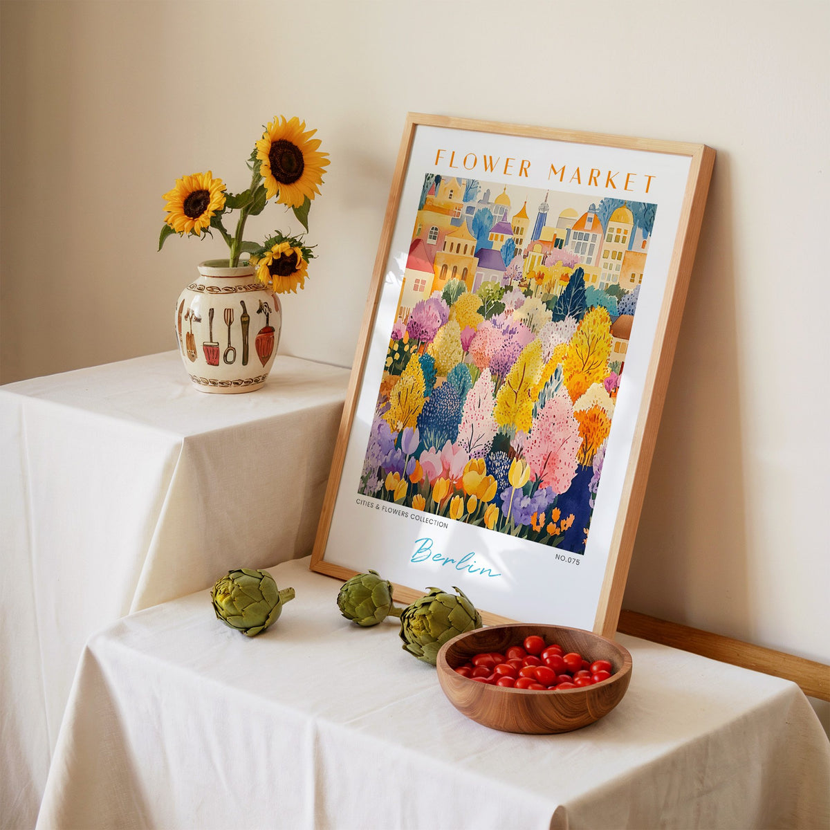 Berlin flower market print in an oak frame leaning on a linen-draped table beside a vase of sunflowers