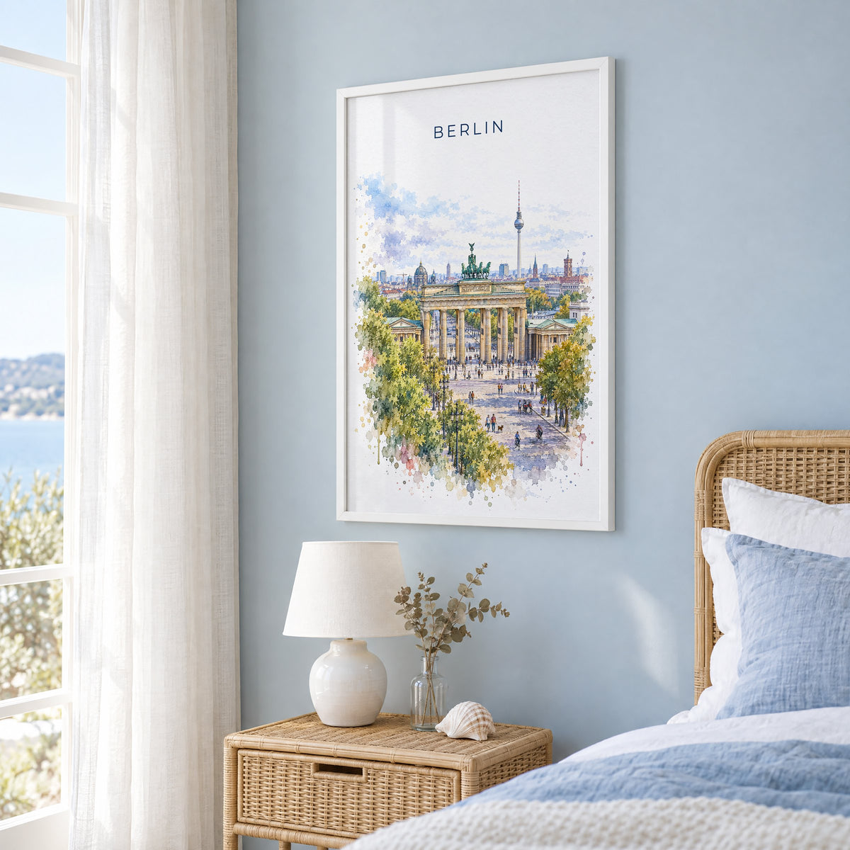 Berlin watercolor print in a white frame on a pale blue wall beside a rattan bed in a coastal bedroom