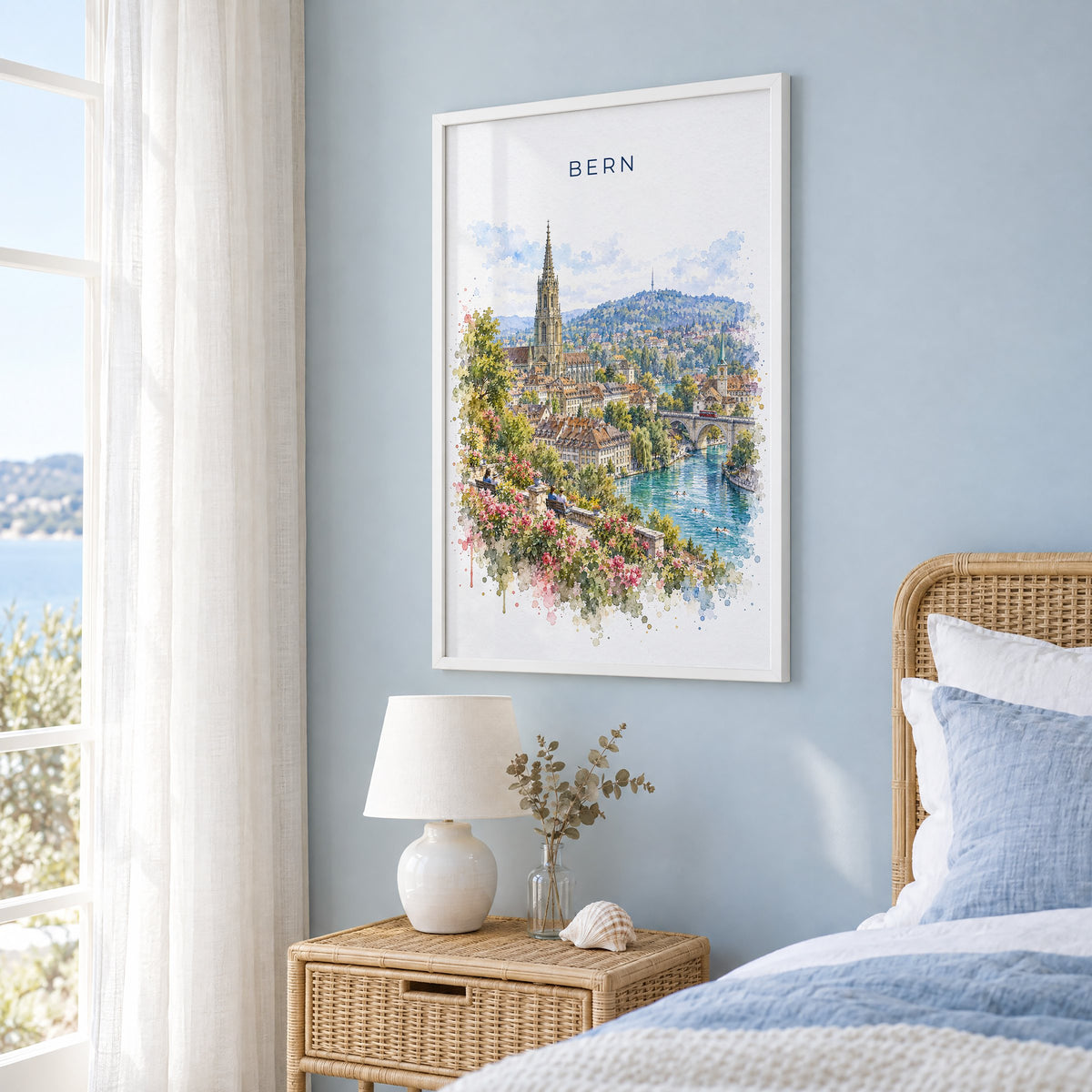 Bern, Switzerland watercolor print in a white frame on a pale blue wall beside a rattan bed in a coastal bedroom