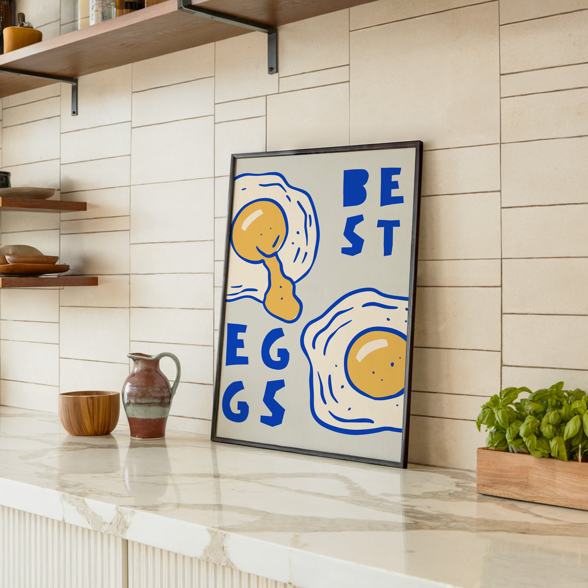 Best Eggs print in a black frame leaning on a marble counter in a tiled kitchen