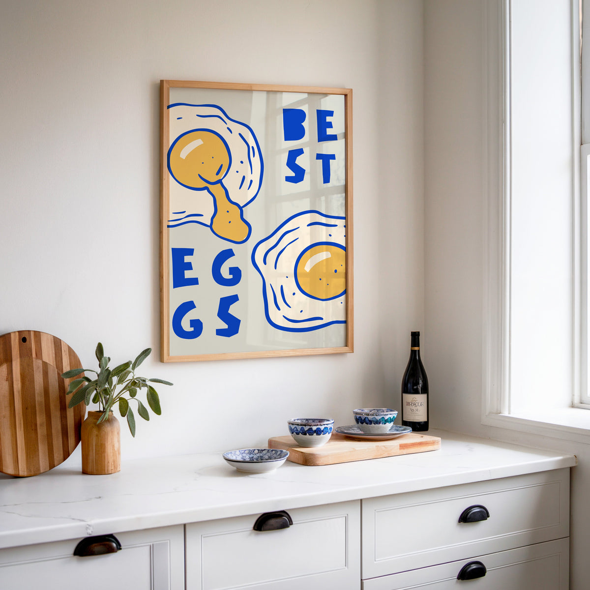 Best Eggs print in an oak frame above a white sideboard with a bottle of wine