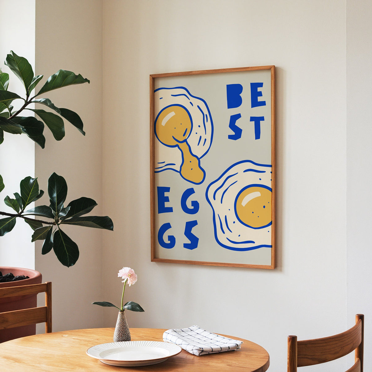 Best Eggs print in a walnut frame above a round table beside a fiddle-leaf fig