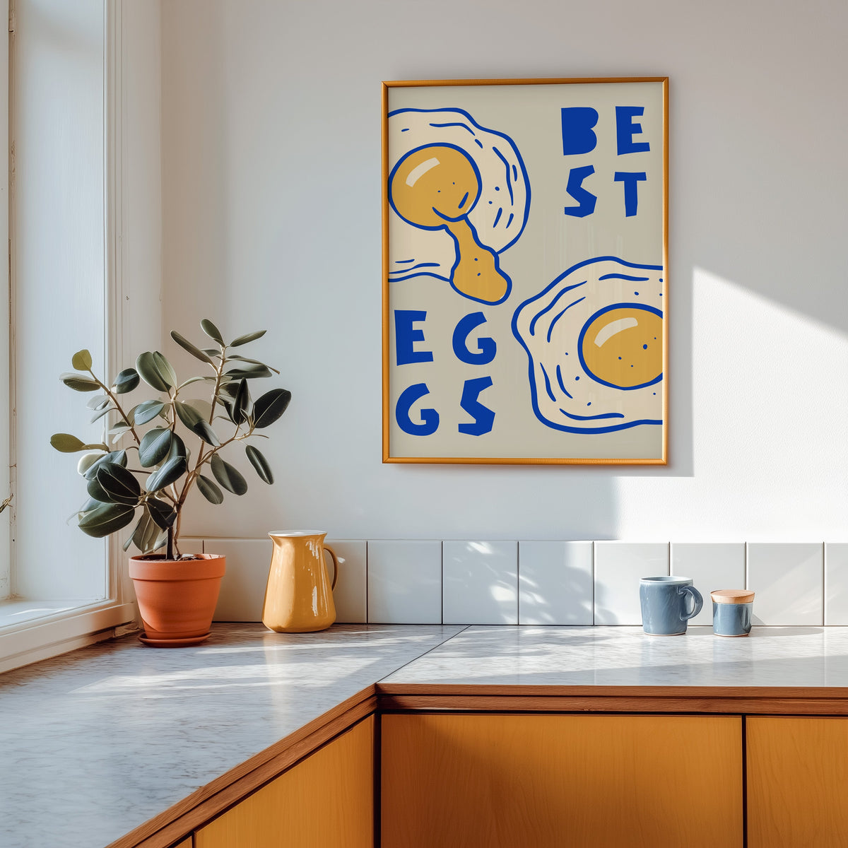 Best Eggs print shown in a gold frame above a marble counter in a tan kitchen
