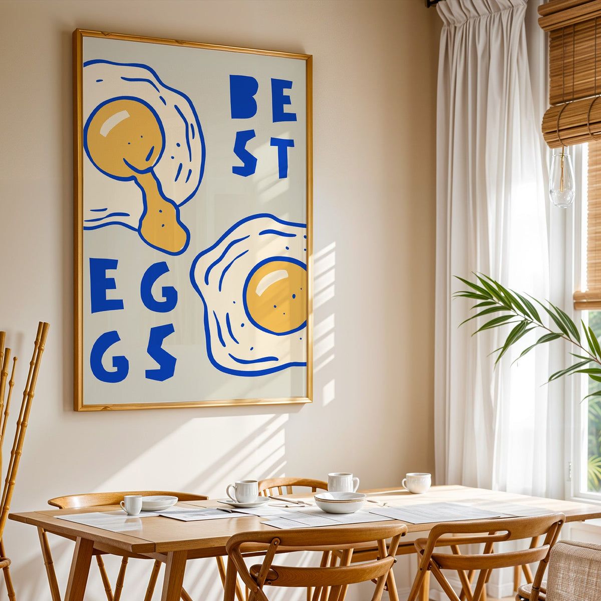 Best Eggs print shown in a gold frame above a breakfast table by a curtained window