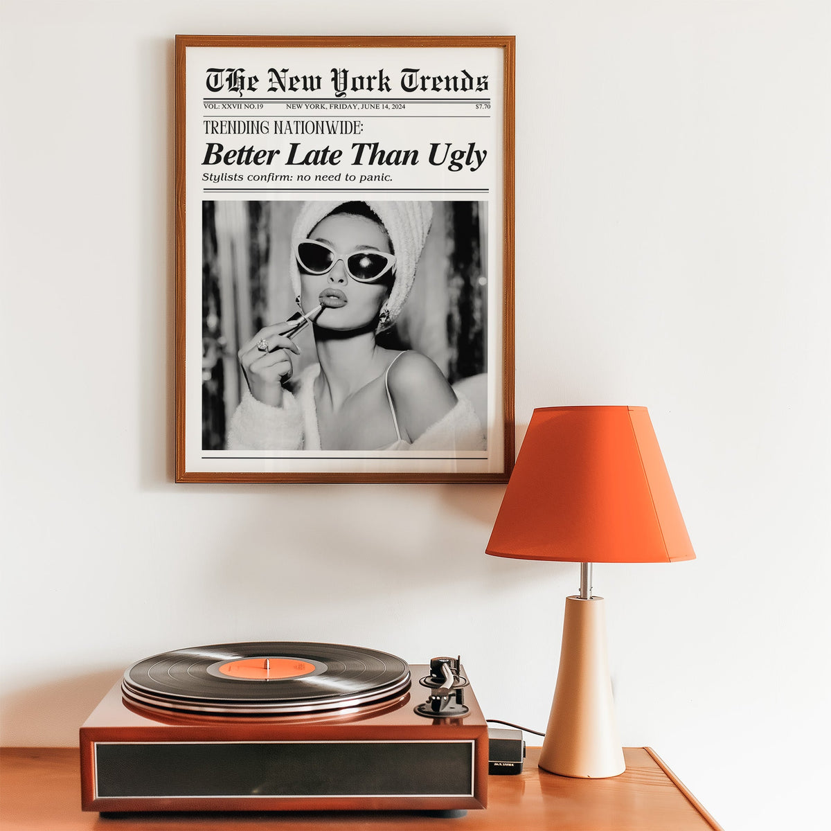 Woman applying lipstick mock newspaper print in a walnut frame above a record player and orange lamp