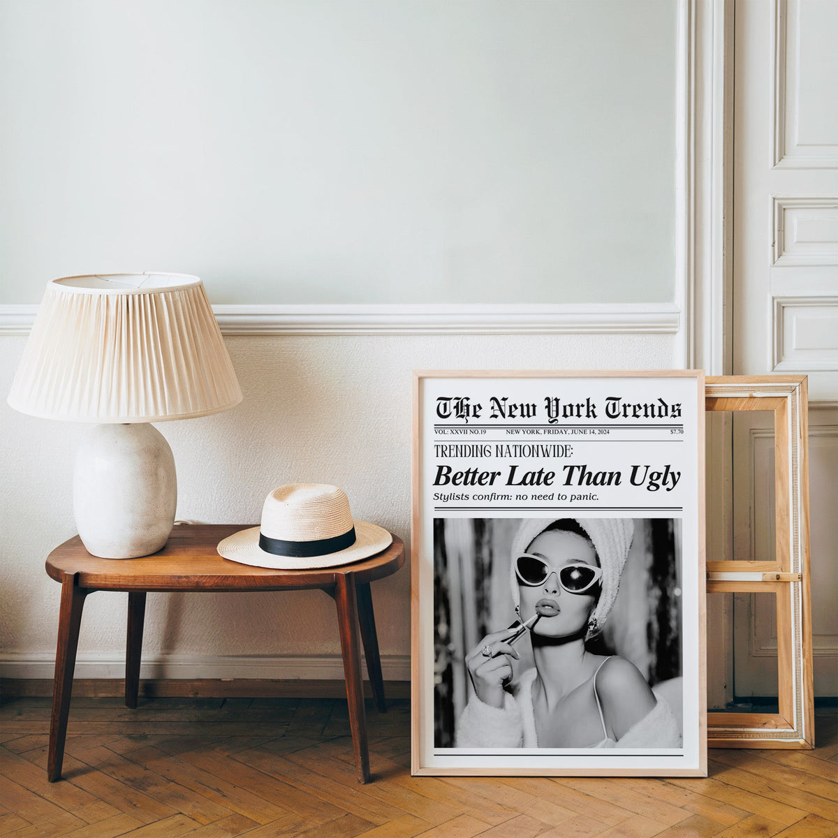Woman applying lipstick mock newspaper print in a pine frame on a wood floor beside a lamp and straw hat