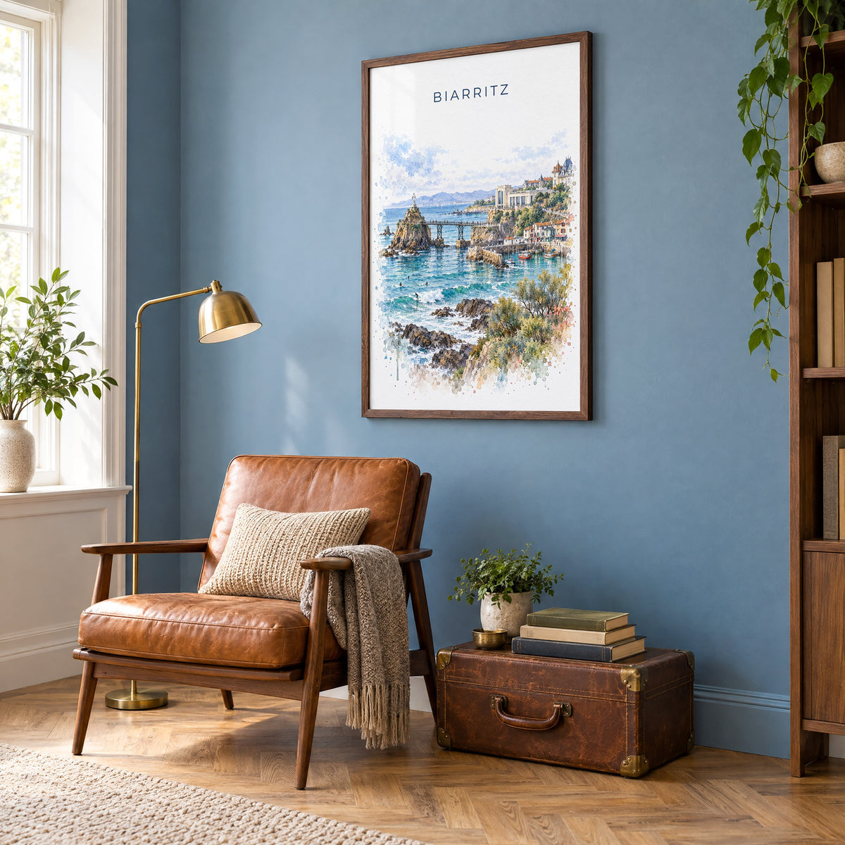 Biarritz watercolor print in a walnut frame on a blue wall above a leather armchair in a reading nook