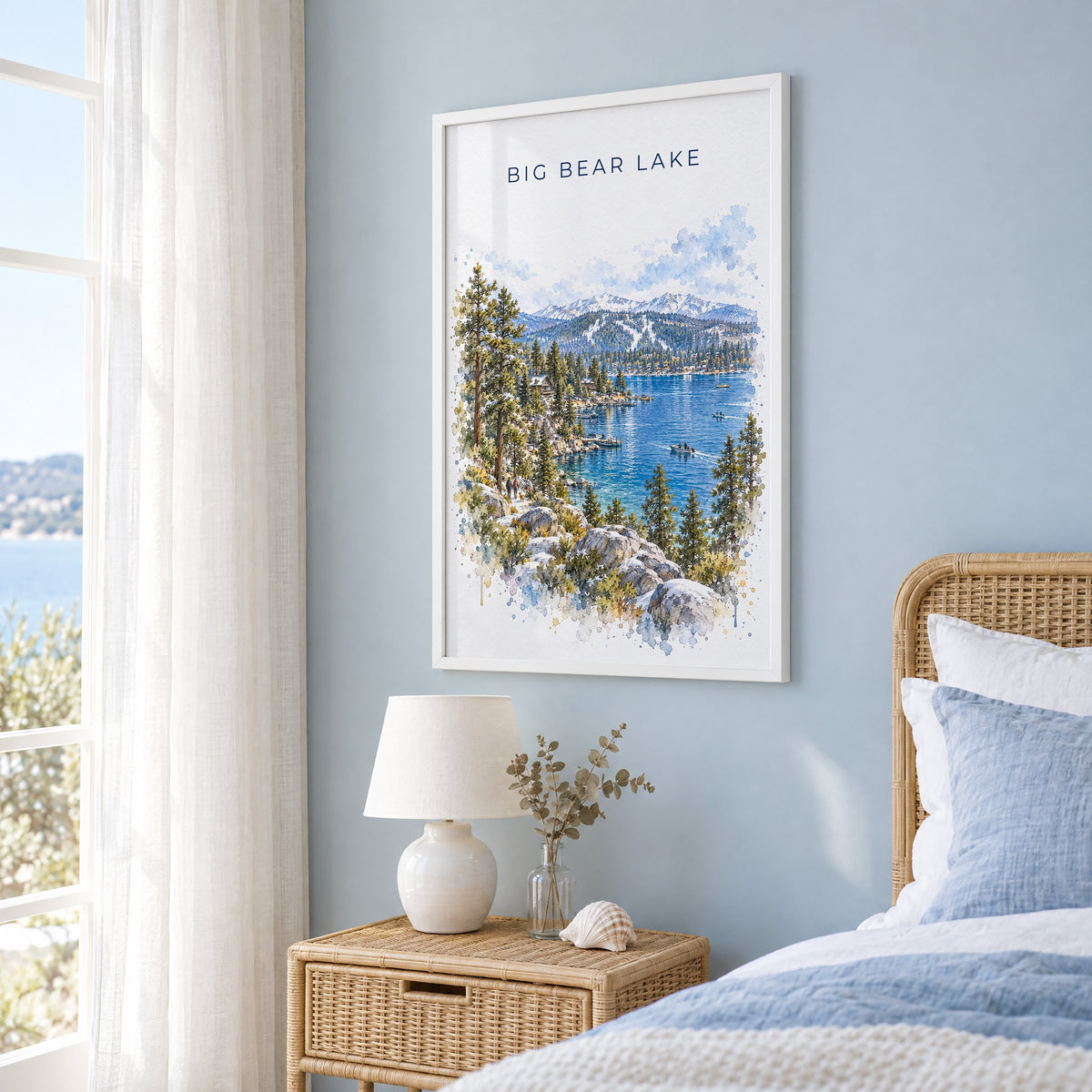 Big Bear Lake watercolor print in a white frame on a pale blue wall beside a rattan bed in a coastal bedroom