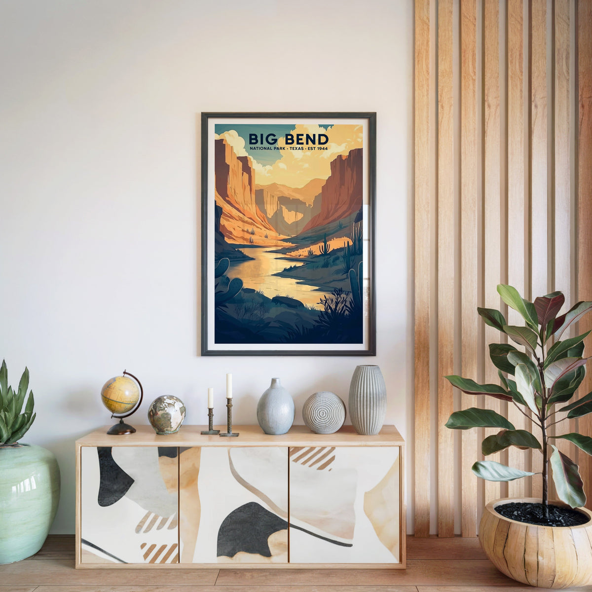 Big Bend National Park print in a black frame above a light wood sideboard with a globe and vases