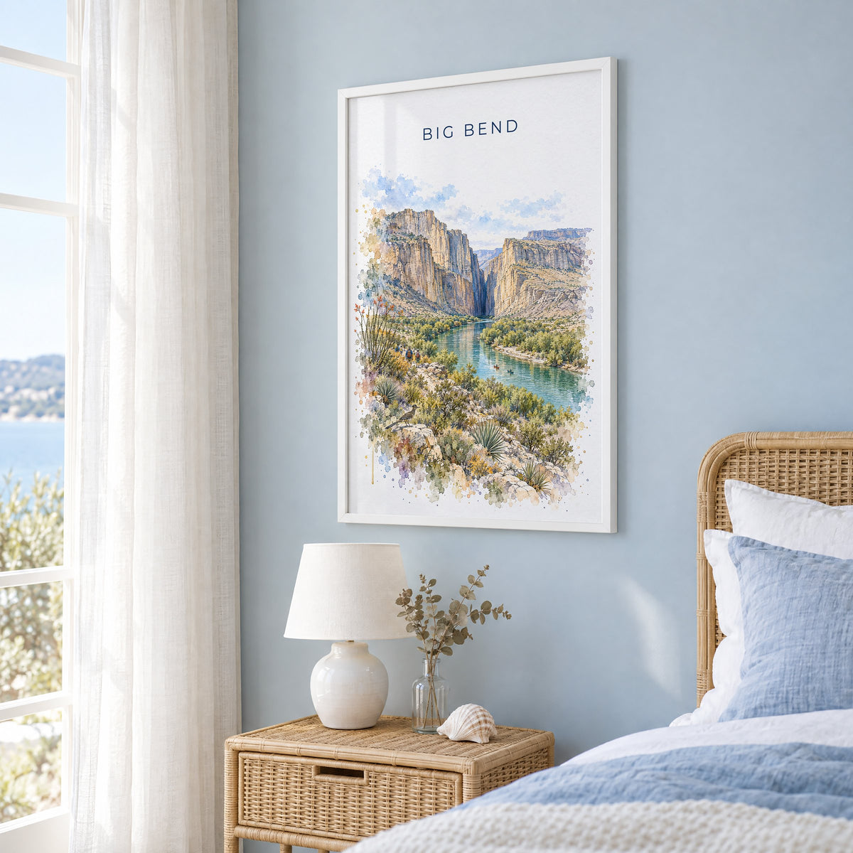 Big Bend National Park watercolor print in a white frame on a pale blue wall beside a rattan bed in a coastal bedroom