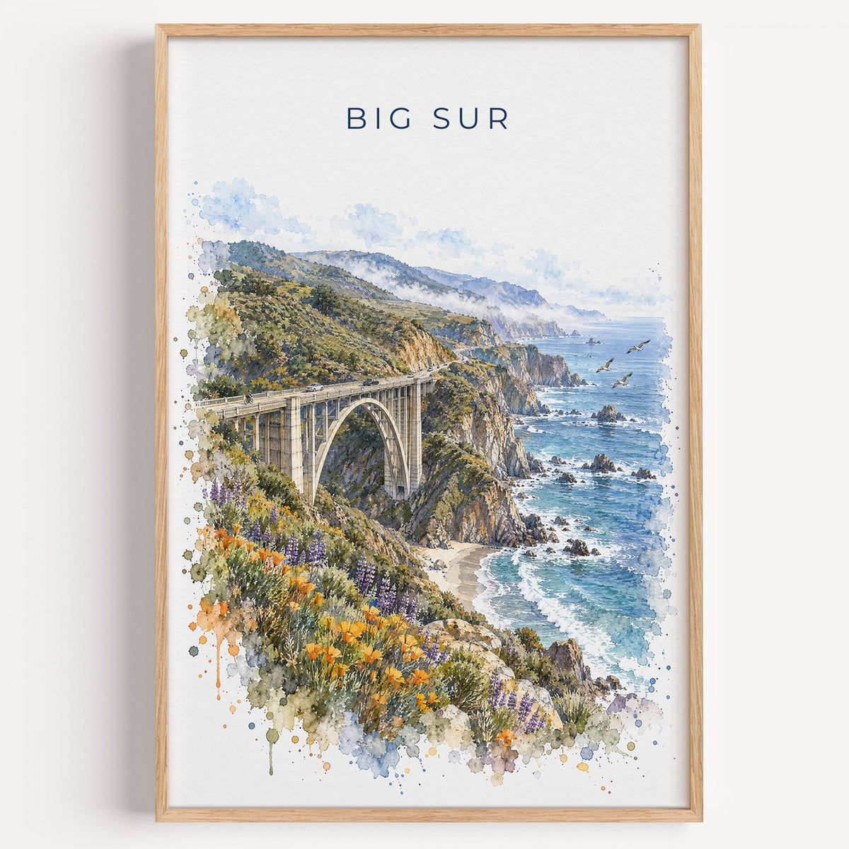 Big Sur watercolor print in a light oak frame on a plain white wall