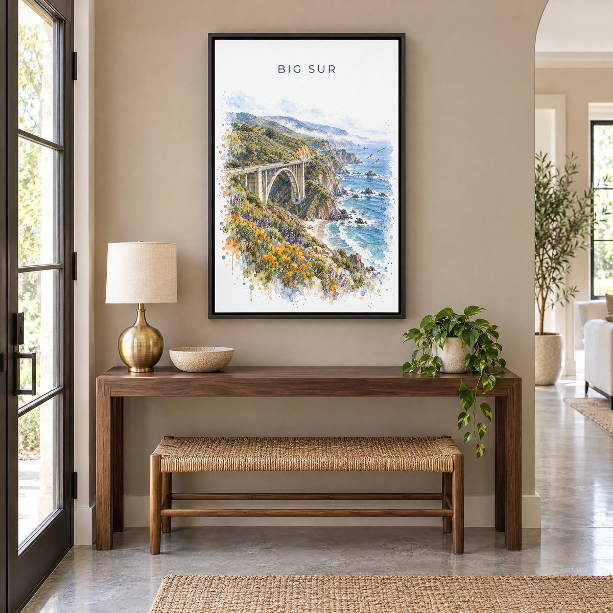 Big Sur watercolor print as a black floater canvas above a walnut console and woven bench in an entryway